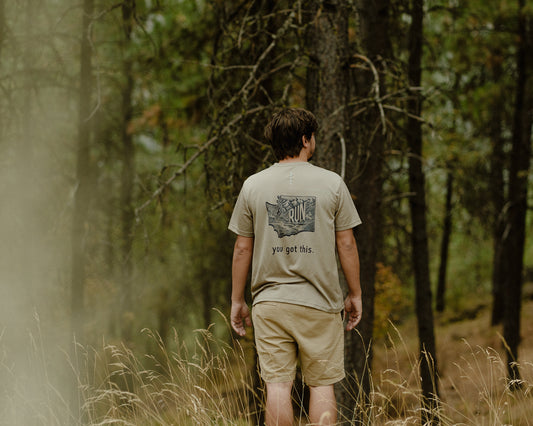 A runner wearing a 'Run PNW' shirt with the phrase 'You Got This' stands proudly amidst a scenic Pacific Northwest backdrop, embodying the spirit of running in this unique region.